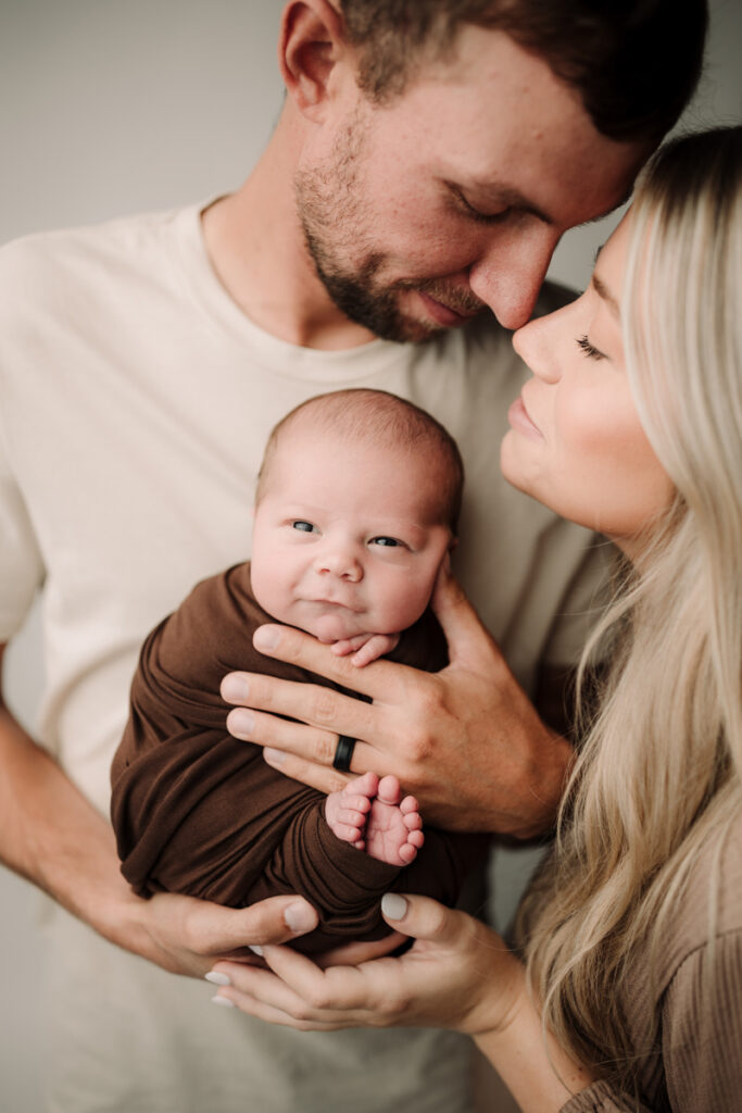 Newborn and Maternity Photographer, a young husband and wife hold their newborn baby together