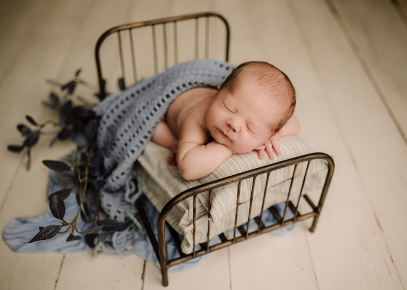 Newborn Baby, a baby sleeps on a tiny bed wrapped in a blue blanket