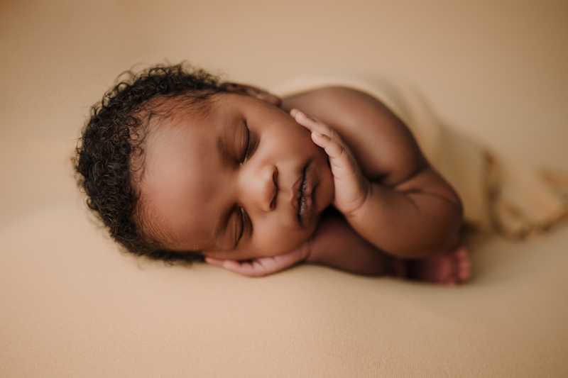 Newborn Photographer, a baby lays sleeping in hi s hands on the blankets